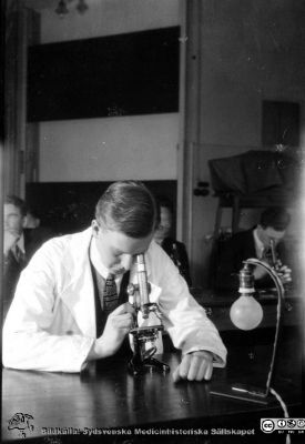 Fotoalbum tillägnat Professor Torsten Hellman från histologkursen 1929.
Fotoalbum tillägnat Professor Torsten Hellman med tacksamhet och vördnad från histologkursen 1929. Bildtext "Ask". 
Rimligen amanuens Olof Ask vid mikroskopet i föreläsningssalen.
- Olof Ask (1909-1988) disputerade i Uppsala 1941 på en avhandling om spina bifida. Från 1956 var han överläkare med ansvar för den medicinska vården på St Lars sjukhus i Lund.
Nyckelord: Anatomiska Institutionen;Histologiska avdelningen;Mikroskopering;Medicinska fakulteten i Lund;Locus Medicus Lundensis;Universitet