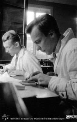 Fotoalbum tillägnat Professor Torsten Hellman från histologkursen 1929.
Fotoalbum tillägnat Professor Torsten Hellman med tacksamhet och vördnad från histologkursen 1929. Bildtext "Henning Lindholm. Helmer Cederlund". 
Rimligen kursdeltagare  i kurslaboratoriet med osäker verksamhet.
- Henning Lindholm (1907-1984) blev efter olika internmedicinska tjänster biträdande överläkare i Kristianstad,1949 - 1956, överläkare i Simrishamn 1957 - 1962 och slutligen överläkare på medicinska kliniken i Kristianstad från 1963.
- Helmer Cederlund (1906 - 1964). Efter olika kirurgiska och internmedicinska tjänstgöringar i Mellansverige blev han 1955 provinsialläkare i Ljungskile.
Nyckelord: Histologiska avdelningen;Anatomiska Institutionen;Medicinska fakulteten i Lund;Locus Medicus Lundensis;Universitet;Kurslaboration