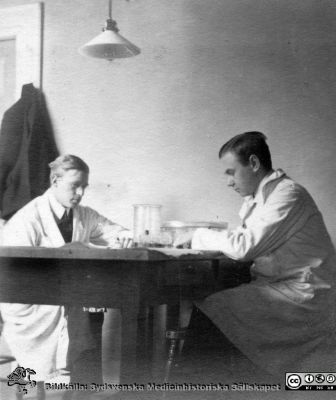 Fotoalbum tillägnat Professor Torsten Hellman från lärjungar under Kursen 1924 - 25
Fotoalbum tillägnat Professor Torsten Hellman från lärjungar under Kursen 1924 - 25. Två unga män i laboratorierockar vid ett bord med glasburkar, rimligen för för hantering och färgning av preparat för mikroskopering. Rimligen är det två kursamanuenser. De är inte identifierade.  Ingen bildtext.
Bildkälla Stiftelsen Locus Medicus Lundensis 250317. Fotograf okänd.
Nyckelord: Histologiska avdelningen;Anatomiska Institutionen;Medicinska fakulteten i Lund;Sydsvenska Medicinhistoriska Sällskapet;Locus Medicus Lundensis;Lärare;Elever