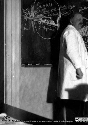 1928 års histologikurs i Lund
Fotoalbum märkt Histologikursen anno 1928. 
Detta album innehåller bilder från dåvarande histologiska avdelningen på anatomiska institutionen i Lund på Biskopsgatan 7. Liksom de övriga i serien skapades det av kursdeltagarna och tillägnades kursledaren professor Torsten Hellman som uppskattning av hans lärargärning. Bilden är inte namnsatt. Den visar professor Torsten Hellman i ljus laboratorierock när han föreläste om innerörats mikroskopiska anatomi, kanske i avdelningens mikroskoperingssal. 
Bildkälla Stiftelsen Locus Medicus Lundensis 250317.
Nyckelord: Locus Medicus Lundensis;Medicinska fakulteten i Lund;Histologiska avdelningen;Sydsvenska Medicinhistoriska Sällskapet;SMHS;Anatomiska Institutionen;Lärare