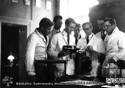 1928 års histologikurs i Lund
Fotoalbum märkt Histologikursen anno 1928. 
Detta album innehåller bilder från dåvarande histologiska avdelningen på anatomiska institutionen i Lund på Biskopsgatan 7. Liksom de övriga i serien skapades det av kursdeltagarna och tillägnades kursledaren, professor Torsten Hellman som uppskattning av hans lärargärning. Bilden är inte namnsatt. Den visar amanuenser och kursdeltagare i kurslaboratoriet där de möjligen blandar vätskor för att tillverka preparat för mikroskopering. 
Bildkälla Stiftelsen Locus Medicus Lundensis 250317.
Nyckelord: Locus Medicus Lundensis;Medicinska fakulteten i Lund;Histologiska avdelningen;Sydsvenska Medicinhistoriska Sällskapet;SMHS;Anatomiska Institutionen;Studenter;Lärare;Kurslaboratorium