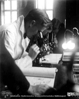 1928 års kurs i histologi i Lund
Fotoalbum märkt Histologikursen anno 1928. 
Detta album innehåller bilder från dåvarande histologiska avdelningen på anatomiska institutionen i Lund på Biskopsgatan 7. Liksom de övriga i serien skapades det av kursdeltagarna och tillägnades kursledaren, professor Torsten Hellman, som uppskattning av hans lärargärning. Bilden visar en av kursamanunerserna, "Eonerna", Hjalmar Sjövall enligt bildtext. Han sitter vid ett kursmikroskop i avdelningens mikroskoperingssal. 
Bildkälla Stiftelsen Locus Medicus Lundensis 250317.
Nyckelord: Locus Medicus Lundensis;Medicinska fakulteten i Lund;Histologiska avdelningen;Sydsvenska Medicinhistoriska Sällskapet;SMHS;Anatomiska Institutionen;Studenter;Lärare