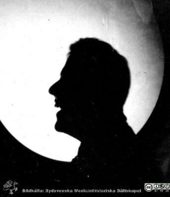 1928 års kurs i histologi i Lund
Fotoalbum märkt Histologikursen anno 1928. 
Detta album innehåller bilder från dåvarande histologiska avdelningen på anatomiska institutionen i Lund på Biskopsgatan 7. Liksom de övriga i serien skapades det av kursdeltagarna och tillägnades kursledaren professor Torsten Hellman som uppskattning av hans lärargärning. Bildtext  "Sjövall".  Silhuett av amanuensen Hjalmar Sjövall mot mikroskopprojektorns runda ljusa skiva, här utan preparat tydligt.
Bildkälla Stiftelsen Locus Medicus Lundensis 250317.
Nyckelord: Locus Medicus Lundensis;Medicinska fakulteten i Lund;Histologiska avdelningen;Sydsvenska Medicinhistoriska Sällskapet;SMHS;Anatomiska Institutionen;Studenter;Lärare