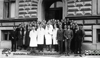 Fotoalbum  från histologkursen 1931.  Bildtext "Histologikursen 1931. ".  Kursfoto på trappan till anatomiska institutionen i Lund. Professor Torsten Hellman i vit rock bakom de fyra amanuensera, även de i vita laboratorierockar.
Längst till vänster bland amanuenserna Gösta Glimstedt (1905 - 1970), från c:a 1943 efterträdare till Torsten Hellman.  Mannen nr 3 från höger i främsta raden är troligen Olle Olsson (1911 - 1999), senare professor i röntgenologi i Lund.
Bildkälla Stiftelsen Locus Medicus Lundensis 250317. Sydsvenska Medicinhistoriska Sällskapet / SMHS. Fotograf okänd.
Nyckelord: Histologiska avdelningen;Anatomiska Institutionen;Locus Medicus Lundensis;Medicinska fakulteten i Lund;Medicine studerande;Elever