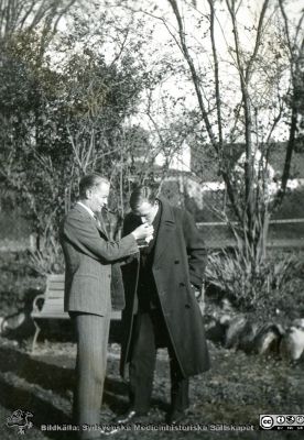 Fotoalbum  från histologkursen 1931.  Bildtext "Rast". "Barnen" i anatomiska insitutionens park. Löven har börjat falla. Byggnader skymtar bakom träden med glesa löv. Kanske är det "Reimers Hollywood" som tänder en studentkamrats cigarrett.
Bildkälla Stiftelsen Locus Medicus Lundensis 250317. Sydsvenska Medicinhistoriska Sällskapet / SMHS. Fotograf okänd.
Nyckelord: Medicine studerande;Histologiska avdelningen;Anatomiska Institutionen;Medicinska fakulteten i Lund;Locus Medicus Lundensis;Universitetet i Lund;Studenter i parken