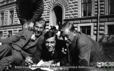 Fotoalbum tillägnat Professor Torsten Hellman med tacksamhet och vördnad från histologkursen 1929. Bildtext saknas. Studenter utanför anatomiska instiutionen i Lund en solig dag.  Bildtext "N. K.". Medicine studeranden framför intrétrappan till anatomiska institutionen i Lund en vårlig men sval dag. Möjligen Carl-Erik Uddenberg till höger närmast kameran. De övriga är okända.
