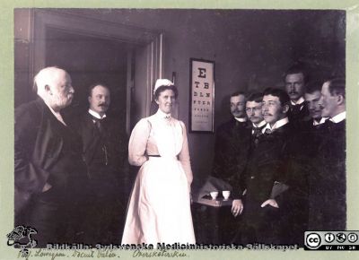 Ögonkliniken i Lund 1903
Foto på ögonkliniken i Lund. Se också bildfil 100911-033. Påskrift på baksidan: "De 3 främsta kandidaterna: Hirschlaff, Helsingborg. Westergård, f.d. Halmstad, Pallin Kristianstad. Den långe bakom: Wallengren, Landskrona. Översköterskan Fröken Löwenadler". Översköterskans efternamn är svårtytt. I databasen "Sveriges Befolkning 1900" från finns en övesköterska Klara Theresia Löwenadler, född 1867 i Eksjö och skriven i Krafts rote i Lunds stadsförsamling. Påskrift på ramens baksida: "Nr 4 fr.v. är Herold Hirschlaff intygar sonen Erik Hjortsjö 16/11 -55". 
Fotot har också funnits i Sydsvenska Medicinhistoriska Sällskapets arkiv och digitaliserades där c:a 2002 för Håkan Westling. Se fil 13Löwegren. Bilden anges där vara tagen 1903, och de tjänstgörande kandidaterna anges heta Gustaf Pallin, Emil Westergård, Herold Hirschlaff, Sven Johansson och Herman Wallengren
En mycket snarlik bild, rimligen från samma fototillfälle, finns publicerad i  'Ur en lundamedicinares minnesbok. Anteckningar gjorda av Michael Kolmodin Löwegren. Med kommentar utgivna av Ynge Löwegren'. Sydsvenska Medicinhistoriska Sällskapets Årsskrift 1971, sid 58 - 72. Fil 030205c.tif.
Nyckelord: Lasarettet;Lund;Universitet;Universitetssjukhus;USiL;Ögon;Oftalmologi;Kurs