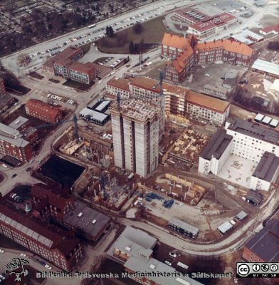 Flygfoto av Blocket i Lund under byggnad, c:a 1965 / 66
Flygbild av bygget av C-blocket i Lund. Det södra av de centrala tornen med hiss-schakt dominerar i bilden. Till höger det redan byggda E-blockets första delar och bakom bygget det också redan färdiga AB-blocket. Överst i bild Gamla Folkskoleseminariet och lasarettsmatsalen. Nederst i bild dåvarande ortopediska kliniken och ögonklinikens tak. - Från ett album gjort av byggfirman SIAB från bygget av C-blocket i Lund 1964 - 1967. Det är tillägnat professor Olle Olsson, en av de starkaste cheferna på sjukhuset vid denna tid, och bevaras på hans gamla klinik / avdelning.
Nyckelord: Lasarettet;Lund;Universitet;Universitetssjukhus;Blocket;Centralbyggnaden;C-blocket;Bygge.