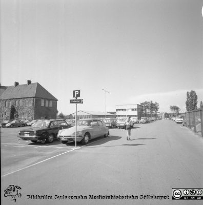 Lasarettet i Lund 1971. Parkeringsplatsen öster om folkskoleseminaret
Sjukhusfotograferna i Lund. Pärm Diverse tagningar. 1971, 1972, 1973. Exteriörer, lasarettsområdet juli 1971. Vy mot nordost på folkskoleseminariets östersida mot sjuksköterskebostäderna. I förgrunden temporära byggnader för bl.a. evakuering för verksamheter vid ombyggnader. Bl a bodde personalavdelningen där en tid. Barackerna revs c:a 1981. Från negativ.
Nyckelord: Lasarett;Lund;Universitet;Universitetssjukhus;USiL;Folkskoleseminarium;Sköterskebostäder;Fysikalisk;Medicin;Sjukgymnastik;Parkering