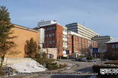 Strålbehandlingens entrédel och gamla onkologiska kliniken, Universitetssjukhuset i Lund. 
Strålningsavdelningen till vänster, onkologiska kliniken i mitten och centralblocket i bakgrunden. Verkstäder i tvåvåningsbyggnaden till höger. Universitetssjukhuset i Lund. Foto i januari 2010.
