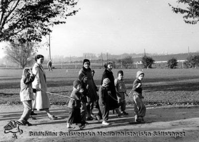 Barnpatienter på promenad i Vipeholmsparken
Bild 51. Vipeholm Barnpatienter. Foto i mitten på 1900-talet. Lund skymtar på horisonten. Höghusen i stadens östra del är ännu inte byggda.
Publicerad på sid 76 i Carlén-Nilsson C, Holmér U (1998) Röster från Vipeholm. pp. 1-127 Stiftelsen medicinhistoriska museerna i Lund och Helsingborg, Lund. Bildtext där: "Barnpatienter på promenad". Foto Omonterat. Notera ledbanden.
Nyckelord: Kapsel 14;Foto;Omonterat;Barn;Barnpatienter;Personal;Vipeholm;Ledband;Koppel