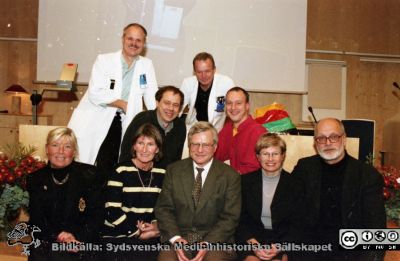 Malmö Allmänna Sjukhus 1999. Temadag på infektionskliniken i Jubileumsaulan, Stig Cronberg sista arbetsdag
Album MAS 1998. IV. 1999. I. Från fotograf Björn Henrikssons samling. 00-10869. 1999. Temadag på infektionskliniken i Jubileumsaulan i samband med Stig Cronbergs pensionering och sista arbetsdag. Han meddelade om bilden bl.a.: 
Längst bak i vit rock Sven Haidl (mustasch). Malmöutbildad, mycket effektiv och kunnig.  Bredvid honom Thorbjörn Prellner, också i vit rock. Chef för infektionsklionikens intensivvårdsavdelning. Svensk mästare i simning liksom hustrun, professor på öronkliniken i Lund. Mycket kunnig och effektiv.
Framför dem från vänster kurator Magnus Andersson, kurator. Uppvuxen i små omständigheter. Folkskola, sedan folkhögskola och socialhögskola. Mycket effektiv och omtyckt av missbrukare. Kunde få tusen åhörare till våra möten. Bredvid honom Niclas Winqvist, ursprungligen sjuksköterska, gick folkhälsoutbildning i Göteborg och blev smittskyddsexpert. Forskade även i Guinea Bissau. 
Nedanför från vänster, sittande: Inga Odenholt, från Uppsala, sedermera professor i infektionssjukdomar. Ewa Wallmark överläkare, expert på hiv och hepatit C. Klarade att hantera också beväpnade missbrukare. Stig Cronberg. Marlene Wullt, disputerad infektionsläkare. Gift med professor Wullt vid urologen i Lund. Hans Bertil Hansson, smittskyddsläkare med administrativ talang. Från negativ.
Nyckelord: UMAS;MAS;Malmö_;Allmänna;Sjukhus;Infektion;Utbildning;Temadag;Uppvaktning;Pensionering
