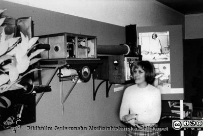 Från den medicinhistoriska utställningen "Vårda - bota" på Kulturen i Lund i september - oktober 1968, 
Medicinhistorisk utställning "Vårda - bota" på Kulturen i Lund i september - oktober 1968, ordnad med anledning av lasarettets 200-årsjubileum. En gammal EKG-maskin på väggen; den kopia av Einthovens maskin som Aron Westerlund hämtade hem och som finns på sid 64 i boken "3 professorer" av Håkan Westling. I bakgrunden bilder från slutet av 1960-talet, visande s.k. kabel-ekg på det då nybyggda centralblocket på Lasarettet i Lund. Kulturens utställningskommissarie Margareta Alin ses vid utrustningen. Jämför bild SMHS2605_000_01, SMHS1027 och SMHS1028. Originalfoto
Nyckelord: Kulturen;Lund;Medicin;Historia;Jubileum;Universitetsklinik;Utställning