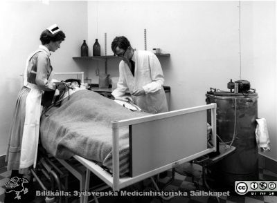 Klinisk dialys. Foto från utställning
Utställning i slutet på 1900-talet på medicinhistoriska museet i Lund visande dialys någon gång på 1960-talet. Den stora plåtcylindern till höger är den tidens dialysapparat, den s.k. Avestanjuren, konstruerad av Nils Alwall. 
Medicinhistoriska museet i Lund. Omärkt omonterat fotografi.
Nyckelord: Dialys;Dialysapparat;Interiör;sjuksköterska;SSSH;läkare;utställning;docka;Medicinhistoriskt;Museum;Lund;Foto;Omonterat;Kapsel 07