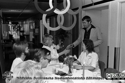 Olympisk guldmedalj till anställd på Lasarettet i Lund
Sjukhusfotograferna i Lund. Pärm negativ, S/V. 1976.	122. Bodil Elg (f. 1937), guldmedaljör vid Paralympics i Toronto sommaren 1976 i bågskytte, gratuleras till sina framgångar på kliniskt kemiska laboratoiret i Lund där hon arbetade. Gratulanten är inköposchefen Bertill Widell. Den hiterste mannen vid bordet är tf klinikchefen i klinisk kemi, docent Bengt Johansson. Från negativ.
Nyckelord: Lasarettet;Lund;Universitet;Universitetssjukhus;USiL;Laboratorium;Guldmedalj;Paralympics;Handikapp;Olympiad