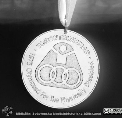 Olympisk guldmedalj till anställd på Lasarettet i Lund
Sjukhusfotograferna i Lund. Pärm Negativ, S/V. 1976.	120. Paralympics-medalj rimligen Bodil Elgs (f 1937, d.2012; bågskytt, guldmedaljör). Hon var anställd på ett laboratorium på sjukhuset. Från negativ.
Nyckelord: Lasarettet;Lund;Universitet;Universitetssjukhus;USiL;Laboratorium;Guldmedalj;Paralympics;Handikapp;Olympiad