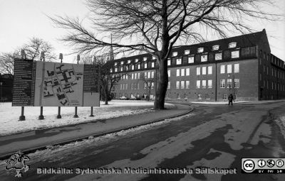 Söderfasaden på gamla kvinnnokliniken,
Sjukhusfotograferna i Lund. Pärm Negativ, S/V. 1976. 32. Söderfasaden på gamla kvinnnokliniken, nu på väg att tömmas när verksamheten flyttade till nyrenoverade lokaler i gamla ortopediska klinikens hus. Allhelgonakyrkan till vänster i bild. En orienteringstavla i förgrunden. Från negativ. 
Nyckelord: Lasarettet;Lund;Universitet;Universitetssjukhus;USiL;Kvinnoklinik;Gynekologisk;BB;KK;Orienteringstavla