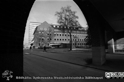 Nya kvinnokliniken (tidigare ortopediska kliniken) från valvet mellan medicinska  och reumatologiska klinikerna. 
Sjukhusfotograferna i Lund. Pärm Negativ, S/V. 1976. 32. Centralblocket i bakgrunden och lasarettskiosken hitom kvinnokliniken. Från negativ. 
Nyckelord: Lasarettet;Lund;Universitet;Universitetssjukhus;USiL;Centralblock;Kvinnoklinik;Gynekologisk;Obstetrik;KK;BB;Förlossning
