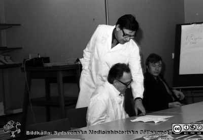 Sammanträde på kirurgiska kliniken i Lund
Sjukhusfotograferna i Lund. Pärm Negativ, S/V. 1976. 14. Sjukvårdsdirektör Åke Haeggström på kirurgiska kliniken i Lund. Professor Stig Bengmark stående, Åke Haeggström sittande. Doc. Bo Eklöf i mörka kläder. Från negativ. 
Nyckelord: Lund;Lasarett;Universitet;Universitetssjukhus;USiL;Kirurgisk;Klinik;Sammanträde;Administration;Sjukvärdsdirektör