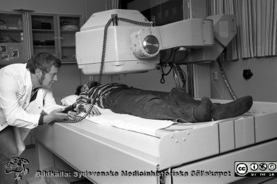 Gammakamera Nuclear-Chicago Pho/Gamma IV
Sjukhusfotograferna i Lund. Pärm Negativ, 1979:2. 125. Foto för doc Ebbe Cederkvist på onkologiska kliniken 79-10-03. Denna gammakamera inköptes cirka 1969-70 med hjälp av donationsmedel från John och Augusta Perssons stiftelse för vetenskaplig medicinsk forskning. Statisterna är Henryk Kupfer (liggande) och Anders Grottefall, båda laboratorieassistenter. Från negativ. 
Nyckelord: Lasarettet;Lund;Universitetssjukhus;USiL;Endokrinologi;Radiologi;Onkologi;Gammakamera;Laboratorium