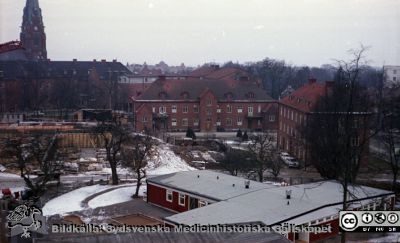 Lasarettet i Lund 1964 - 65. Utsikt mot söder från någon av de övre våningarna på dåvarande barnkliniken (senare kallad Alwallhuset)
Pärm Lasarettsfoto, interiörer och exteriörer m.m. 1958 - 1960. LAS. Exteriör, 61. 23. Foto 1964-65. Nya infektionskliniken har just börjat byggas. Kvar av den gamla infektionsklinikn finns gamla huvudbyggnad (längst till höger i bilden) och en av paviljongerna (i fonden). Allhelgonakyrkan i bakgrunden. Barndaghemmet "Röda Stugan" i bildens nedre högra del. Från negativ, flik 1960
Nyckelord: Lasarett;Lund;Universsitetssjukhus;USiL;Universitet;Infektion;Klinik