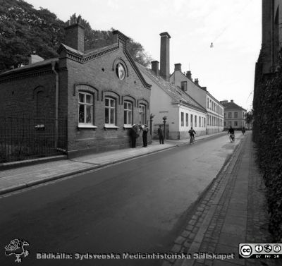 Paradisgatan i Lund vid dåvarande patlogiska institutionen, västerut, 1958
Pärm Lasarettsfoto, interiörer och exteriörer m.m. 1958 - 1960.  Patologiska institutionens vaktmästarbostad / annex närmast kameran. Cura posterior därnäst och sedan dåvarande hudkliniken. 
Nyckelord: Lasarettet;Lund;Universitetssjukhus;USiL;Patologisk;Klinik;Hud;Dermatologi;Venereologi