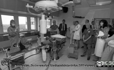 Invigning av ortopediska klinikens operationsavdelning efter renovering, 1986-08-29
Pärm Negativ S/V, färg-1986. 79. Från vänster ses den fullt sterilklädda operationssköterskan Margareta Bråhäll (sedermera chef på operationsavdelningen) som gör någon sorts magisk gest, den legendariske vaktmästaren Rolf Olsson, professor Göran Bauer, sjukhusdirektör Kurt Roos, doc. K.G. Thorngren, doc. Lars Lidgren, professor Pål Benum på besök från Trondheim och flera okända. Informationssekreterare Lena Åsberg längst till höger med stor vit handväska och anteckningsblock i handen. Från negativ. 
Nyckelord: Lasarett;Lund;Universitetssjukhus;USiL;Ortopedi;Operation;Kirurgi;Invigning