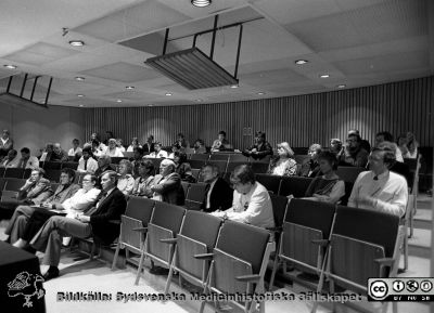 Disputation på kirurgiska kliniken i Lund 1987
Sjukhusfotograferna i Lund. Pärm Negativ, Dia, 1987. 70/1987. Auditoriet när Mogens Bugge disputerade på kirurgiska kliniken i Lund 1987. På första raden sitter betygsnämnden, från vänster docent Claes Henrik Florén (medicinska kliniken, Lund), docent Ingvar Karlberg (kirurg från Göteborg), okänd person i vit rock samt docent Carl-David Agardh (medicinska kliniken i Lund).
På andra raden i publiken  sitter Bengt Jeppsson längst till höger, och till vänster om honom Torsten Holmin, båda kirurger i Lund. Bakom Jeppsson sitter Torbjörn Jonung, också han kirurg i Lund. Bengt Falck sitter näst längst till vänster på fjärde raden. Från negativ. 
Nyckelord: Lasarettet;Lund;Universitetssjukhus;USiL;Disputation;Utbildning;Avhandling;Kirurgisk;Klinik