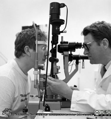 Professor Berndt Ehinger 1987 
Sjukhusfotograferna i Lund. Pärm Negativ, Dia, 1987. 95/87. Professor Berndt Ehinger undersöker 1987 en ung man (en statist) i ett kornealmikroskop på ögonkliniken i Lund. Från negativ. 
Nyckelord: Lund;Lasarettet;Universitetssjukhus;USiL;Forskning;Laboratorium;Ögon;Klinik;Oftalmiatrisk;Oftalmologisk