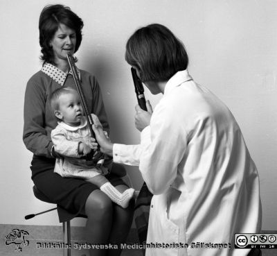 En ögonläkare (troligast docent Elisabeth Stigmar) mäter refraktionen på ett litet barn med skiaskopi
Sjukhusfotograferna i Lund. Pärm Svart-vita neg. 1987.128/-87. Mamman är ortoptisten Janet Hall Lindberg och barnet är möjligen hennes dotter Emma, född 1986-12-25. Foto i september 1987.  Från negativ.
Nyckelord: Laboratorium;Lund;Universitetssjukhus;USiL;Ögon;Klinik;Oftalmiatrisk;Oftalmologisk;Barn;Refraktionering