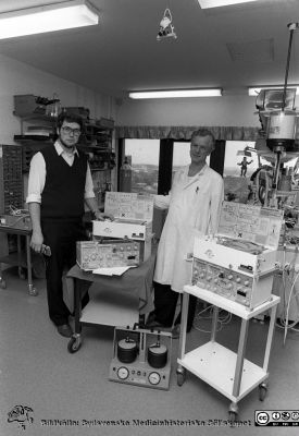 Professorn i medicinsk teknik Nils Gunnar Holmer och anestesiologen, docent Lars Nordström, med ett par ServoVentilatorer.
Sjukhusfotograferna i Lund. Pärm Svart-vita neg. 1987. 146/87.  Foto i januari 1988.
Nyckelord: Lasarettet;Lund;Universitetssjukhus;USiL;Anestesi;Medicinsk;Teknisk;Klinik;Avdelning;MTA;Ventilator;Respirator