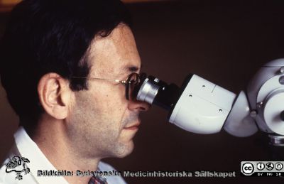 Professorn i klinisk genetik, Felix Mitelman, vid sitt mikroskop.
Pärm Lasarettsfotograferna, gamla färgbilder 1. 43.  Foto troligen på 1980-talet. Från positiv.
Nyckelord: Lasarettet;Lund;Laboratorium;Universitetssjukhus;USiL;Klinisk;Kliniskt;Genetik;Genetiskt