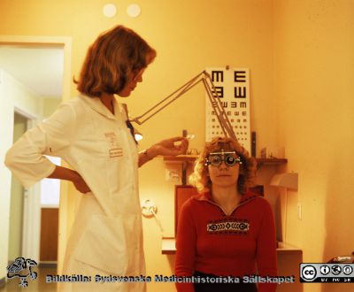 Oftalmologassistenten Anna Ising Glöck refraktionerar en statist, en sekreterare på ögonkliniken i Lund
Pärm Lasarettsfotograferna, gamla färgbilder, Lund. 2. 15. Ö, 24x30. Foto på 1980-talet, troligen i samband med starten av ögonkliniken B. Från positiv.
Nyckelord: Lasarettet;Lund;Universitetssjukhus;USiL;Ögon;Oftalmologi;Oftalmiatrik