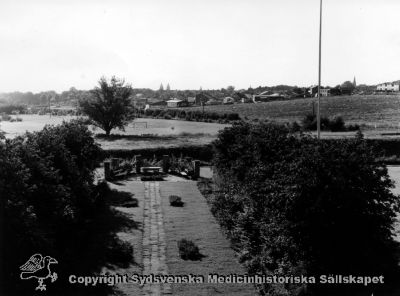 Utsikt västerut över den stensatta parkgången, mot Lund
Vipeholm exteriört. Utsikt västerut, mot Lund, från administrationsbyggnaden. 1900-talets mitt, före 1950-talet då motorvägen byggdes. Foto Omonterat
- Bild SMHS1633 är samma vy, tagen ett par decennier tidigare, under 1930-talets sista halva, när sjukhuset var nybyggt.
Nyckelord: Vipeholm;Exteriört;Utsikt;Västerut;Lund;Administrationsbyggnad;Parkgången