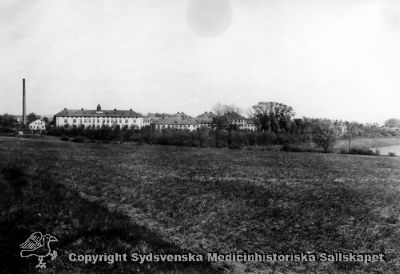 Vipeholms sjukhus från väster i mitten av 1900-talet.
Vipeholm exteriört, vy från väster. Motorvägen förefaller ännu inte vara byggd, men träd och buskar är relativt stora. Därför sannolikt från mitten av 1900-talet, senast mitten av 1950-talet då motorvägen väster om sjukhuset byggdes. Foto Omonterat
Nyckelord: Vipeholm;Exteriört;Kapsel 15;Foto;Omonterat