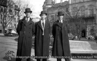 Tre herrar (vårdare på Vipeholms sjukhus?) på Bantorget i Lund, med Grand Hotel i bakgrunden.
Vipeholm personal? Bantorget i Lund. Foto Omonterat.
Klädseln och attributen anger att bilden är tagen i mitten på 1900-talet: Hatt, pipa och trenchcoat / paletå.
Nyckelord: Kapsel 16;Vipeholm;Vipeholm;Bantorget;Lund