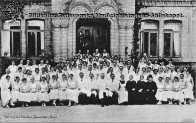 Prof. Gustaf Petrén med kirurgiska klinikens anställda 1923
Kirurgiska kliniken, Lasarettet i Lund: Prof. Petrén med anställda 1923. Håkan Westling skrev 2010-07-25 " På Petréns hö sida troligen Nils Liedberg. Ovanför och till höger troligen Alf Sjövall och på hans vä sida Eric Millbourn". Anders Biörklund skrev 2020-12-05 "Läkaren, som står precis ovanför GP : kan det vara Sommar Bruzelius, som senare blev kirurgchef i Västerås?"
Per-Olof Mattsson i Lomma identifierade 2013 mannen i ljusa kläder längst till vänster i bilden som sin morfar, Jöns Christensson. Denne var sjukhustjänare eller vaktmästare från början av seklet till pensionen. Trol. sofiasyster Ebba Lagström som, nr 2 på bilden åt hö från Petrén. Efter tryckt vykort.
Nyckelord: Kapsel 01;Lasarettet;Lund;Södra;Område;Kirurgi;Kirurgisk;Klinik;Personal;Petrén;Gustaf;Lagström;Ebba;Nils;Liedberg;Eric;Millbourn;Alf;Sjövall