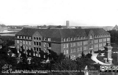 Medicinska kliniken i Lund, 1920-talet
Reprofoto av vykort av medicinska kliniken vid Lasarettet i Lund, fotograferat från Allhelgonakyrkans torn. Fasader mot väster och söder. Automobilen framför huvudingången förefaller vara från tidigt 1900-tal, och kliniken byggdes 1918, så rimligen är den tämligen nybyggd på bilden. Murgrönan har hunnit upp en dryg våning  på västerväggen, så den är nog minst ett par år gammal.
Nyckelord: Lasarettet;Lund;Universitet;Universitetssjukhus;USiL;Medicinsk;Klinik;Vykort