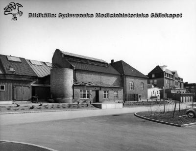 Panncentralen från år 1918 vid Lasarettet i Lund, en del av sjukhusets verkstäder när bilden togs.
Den ursprungliga panncentralen ersattes av en ny längre norrut, färdig 1957. Den stora skorstenen är riven på bilden, och bara basen står kvar som ett tvåvånings runt torn. Bilden bör alltså vara tagen tidigast 1957, kanske både ett och två decennier senare. Huset byggdes till med mera verkstadslokaler i slutet på 1900-talet, men revs slutligen 2010/2011 för att ge plats åt en stor tillbyggnad till onkologiska kliniken. Foto i Lasarettsarkivet. 

Nyckelord: Kapsel 03;Regionarkivet;Lasarettet;Lund;Panncentral;Verkstad;Service