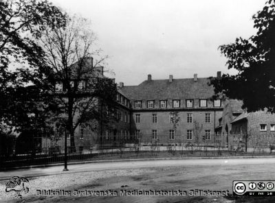 Entrébyggnaden till södra lasarettsområdet från år 1918
Man ser envåningsbyggnaden med ingång och kontorslokaler, trevåningsbyggnaden med kirurgpolikliniken. Vy från öster från korsningen år  2011 mellan  Biskopsgatan och Sandgatan. 
Nyckelord: Kapsel 17;Lund;Lasarettet;Söder;Södra;Lasarett;Område