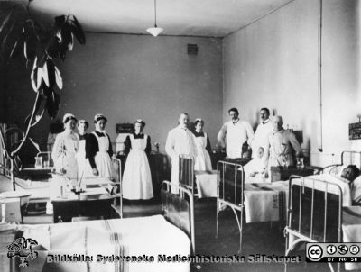 Professor Ribbing på rond i gamla medicinska kliniken år 1910
Nu finns elektrisk belysning och värmeledning. Kaminer och kakelugnar togs bort här år 1904. Avdelningssköterskan Laura Pedersen utexaminerades med den första SSSH-kursen år 1905. Märk de svarta sängtavlorna, påskrivna med krita. Efter reprofoto av foto, tillhörigt Södra Sveriges Sjuksköterskehem. Publicerat i Flaum 1968, sid.199.
Nyckelord: Lasarettet;Lund;Södra;Gamla;Medicinsk;Klinik;1910;Centralvärme;Elektriskt;Elektricitet;Laura;Pedersen