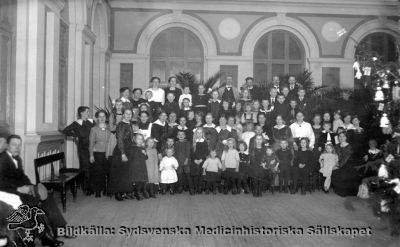 Julfest för personalen på St Lars sjukhus i Lund
Påskrift: "Julfest, i matsalen S:t Lars, på Asylen. 1919-20? "Aslylen" lades formellt sett ned 1910 och blev västra sjukhuset vid Lunds Hospital, men namnet "Asylen" levde likväl länge kvar. Vykort. Originalfoto. Ej monterat
Nyckelord: Kapsel 20;Lund;St Lars;Personal;Kalas;Jul