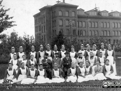 Personal från Asylen samlade år 1895. 
Från kapsel 20 med bilder från St Lars i Lund. Påskrift: "Kv. asyl 1895". Originalfoto.  Monterat. Asylen (senare St Lars Västra Sjukhus) var då alldeles nybyggt.
Nyckelord: St Lars;Lund;Personal;Kapsel 20;Mentalsjukhus