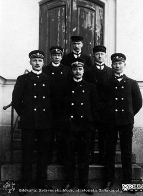 Manliga mentalvårdare 1908
Kapsel 21 med bilder från St Lars. Påskrift: "Den manliga personalens uniformer (Uppsala 1908). Obs. "gradbet.". Vykort skickat till Sjukskötaren Herr N.N. Svensson, Hospitalet, Lund, daterat Uppsala 8/7 1908. 
Nyckelord: Kapsel 21;St Lars;Lund;Uppsala;Mentalvårdare