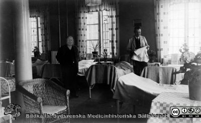 Överskötare Wahlund, avd VB, västra sjukhuset samt en patient 
Kapsel 22 med bilder från St Lars i Lund. Originalfoto. Publicerad på sid 119 i Truedsson 1929. Påskrift där: Interiör från orolig övervakning". Ej monterat
Nyckelord: Kapsel 22;St Lars;Lund;Interiör;Personal;Mentalvårdare