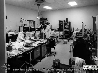 Onkologiska kliniken i Lund i slutet på 1980-talet
Ola Terje låda A bild 16/2. Slutet på 1980-talet. Onkologiska kliniken i Lund. Hypertermibehandling. Fysiker Per Nilsson till vänster, Gull-Maj Aldén vid patienten och dr Claes Ebbe Lindholm bortom. 
Nyckelord: Terje;1980-talet;Onkologi;Klinik;Interiör