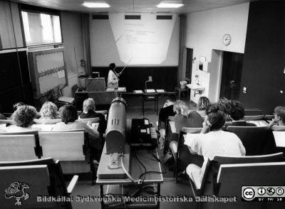 Onkologiska kliniken i Lund. Ingrid Terje föreläser i onkologiska klinikens föreläsningssal.
Foto Ola Terje låda A bild 16/1. Slutet på 1980-talet. 
Nyckelord: Terje;FÃ¶relÃ¤sning;Undervisning;Kursen;Onkologi;Klinik