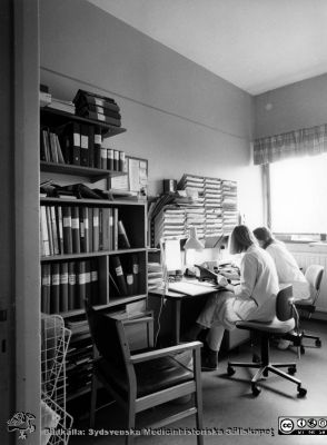 Onkologiska kliniken i Lund. Expedition. Möjligen dr. Eva Ståhl till vänster i bilden.
Foto Ola Terje låda A bild 49/8. Slutet på 1980-talet. 
Nyckelord: Terje;Onkologisk;Onkologi;Klinik;Lund;Interiör;1980-talet;Expedition