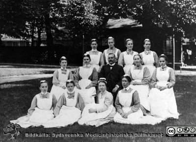 Dr Emil Lundström och sköterskor c:a år 1905 på medicinska kliniken i Lund 
Kapsel 29	D:r Emil Lundström - omkr. 1905: amanuens o underläk. Med .klin. Lund., stadsdis. Läk. Malmö. Död i hjärtinfarkt 1926. Kopia av kort i ägo hos D:r Bengt Lundström 12/7.68 (Vänersborg). Foto: Lina Jonn, Lund. Baksida: Personal LL. Originalfoto. Monterat. Sofiasystern bör vara Inez Oom (sittande, svart mössband). Mycket lik bild SMHS505_000_01, troligen dublett.
Nyckelord: Kapsel 29;Personal;Park;Medicin