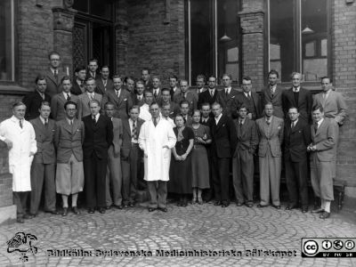 Kurs i patologi i mitten på 1900-talet
Kapsel 30. Påskrift: "Utanför patologen Lund. Utb. Läkare". Kursfoto med Arvid Lindau (i vit rock mitt i iblden). Studenten till vänster och bakom de två damerna är säkerligen  Nils-Johan Nilsson f. 1915? underläkare med klin Lund, sedan professor i klinisk fysiologi i Göteborg. Sysslade med oximetri. Ett huvud skymtar till höger bakom en man med näsduk i bröstfickan är nog Hans Krook, Öl i medicin i Vänersborg, Originalfoto av P. Bagge i Lund. Ej monterat
Nyckelord: Kapsel 30;Professor;Undervisning;Studenter